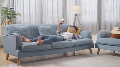 Teen Boy Using Smartphone Taking Selfie While Lying On Sofa In The Living Room Stock Footage 247983386