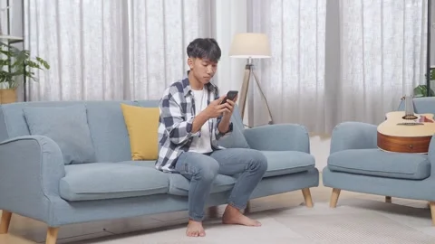 Teen Boy Using Smartphone While Sitting On Sofa In The Living Room At Home Stock Footage 247983538