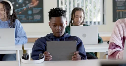 Teen classmates working in class, navy-hoodie teen holding tablet, others typing Stock Footage 341029310
