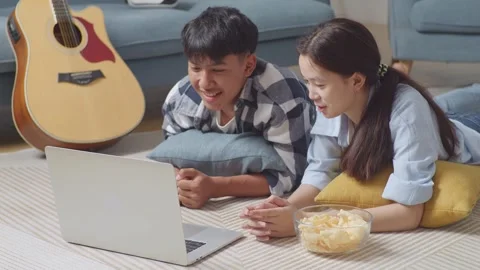 Teen Couple Using A Laptop While Lying On Carpet On The Floor At Home. Watching Stock Footage 247973628