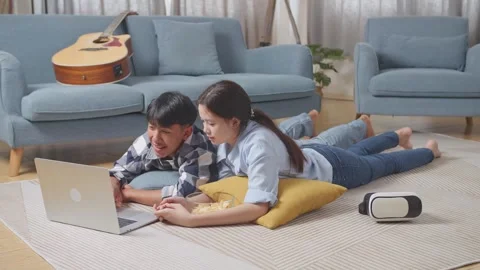 Teen Couple Using A Laptop While Lying On Carpet On The Floor At Home. Watching Stock Footage 247975342