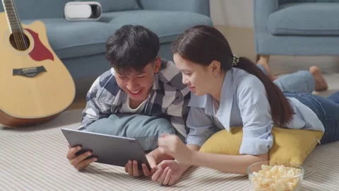 Teen Couple Using Tablet While Lying On Carpet On The Floor At Home. Watching Stock Footage 247973412