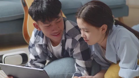 Teen Couple Using Tablet While Lying On Carpet On The Floor At Home Stock Footage 247974426