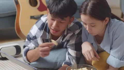 Teen Couple Using Tablet While Lying On Carpet On The Floor At Home. Eating Stock-Footage 247974496
