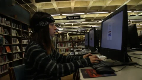 Teen with facemask down in library on computer Stock Footage 134680283