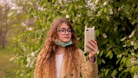 Teen girl in glasses with protective mask calling on smartphone Stock Footage