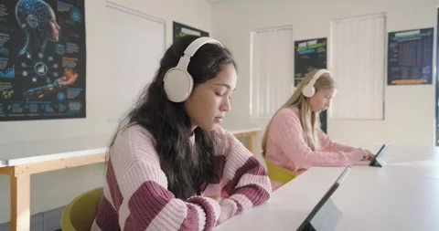 Teen girls using tablets at table headphones, camera moving closer leading teen Stock Footage 340898633