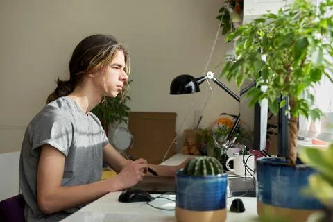 Teen guy at home working on computer, using graphics tablet to work with images Stock Photos