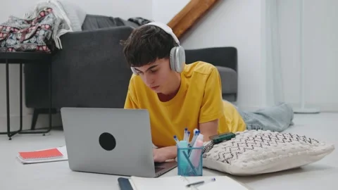 Teen studying on the floor with laptop while wearing headphones in modern indoor Video stock 305774884