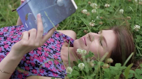Teen studying lying down on grass outdoor. Woman student reading book Video stock 65937775