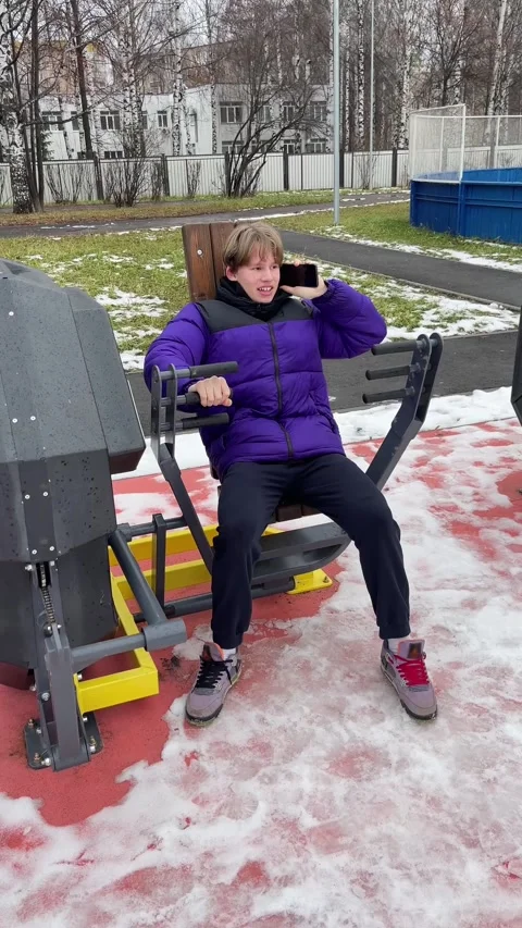 Teen is talking on phone while doing exercises on outdoor gym equipment Stock Footage 309300801