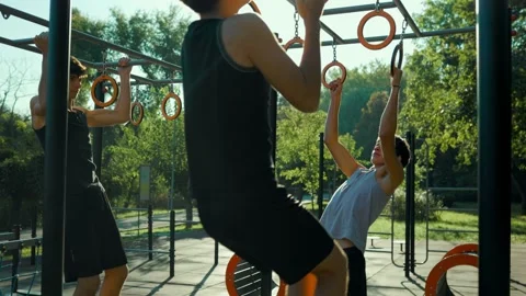 Teen youth group doing pull ups on gymnastic rings during outdoor training. Stock Footage 346140021