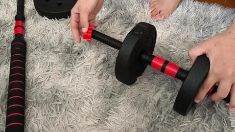 A teenage boy assembles an adjustable barbell, a dumbbell. The guy regulates the Stock Footage 320523158