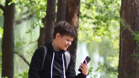 Teenage boy with a backpack in the forest, taking a selfie on a smartphone Stock Footage 274882250