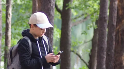 Teenage boy with a backpack in the forest, taking a selfie on a smartphone Stock Footage 274884545