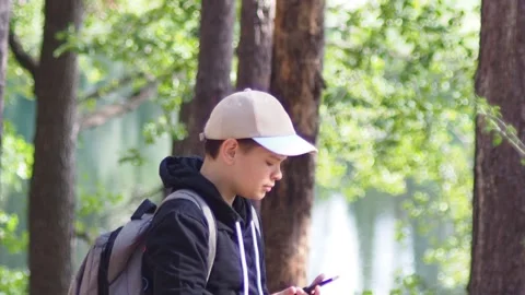 Teenage boy with a backpack in the forest, taking a selfie on a smartphone Stock Footage 274884548