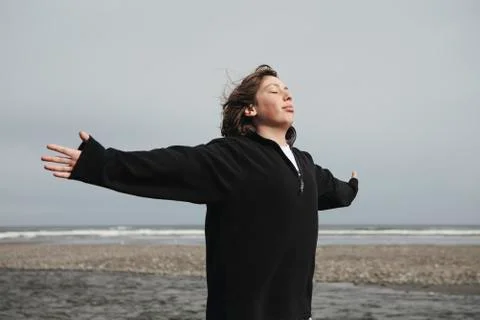 Teenage boy on beach with arms outstretched towards breeze, ocean in distance Stock Photos