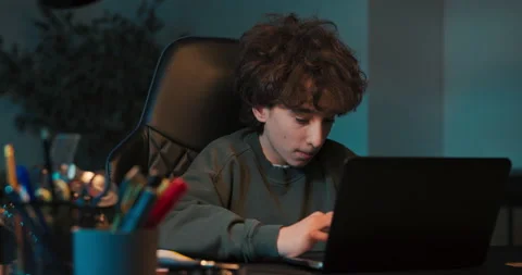 Teenage boy doing homework using computer sitting by desk in room alone Stock Footage 200866765