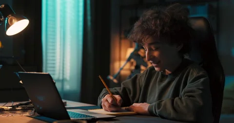 Teenage boy doing homework using computer sitting by desk in room alone Vídeo Stock 200872961