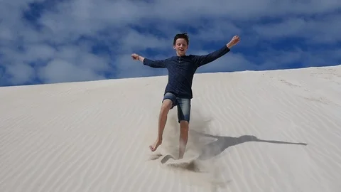 Teenage boy jumping down soft white sand dune Stock Footage 106938609
