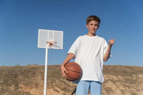 Teenage boy looking at camera while posing with basketball ball at an outdoor Fotos Stock