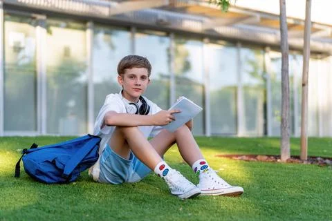 Teenage boy looking at camera while sitting on grass with a notebook and Foto stock