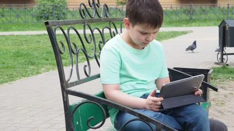 Teenage Boy On Park Bench Using Laptop And Digital Tablet chatting Stockbeeldmateriaal 154795014