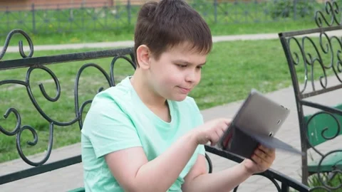 Teenage Boy On Park Bench Using Laptop And Digital Tablet chatting Stock Footage 154811014