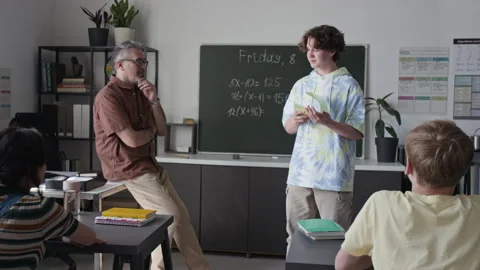 Teenage Boy Presenting Math Solution to Middle Aged Teacher in Classroom Stock Footage 339667957