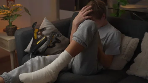 Teenage boy reading a book while recovering at home with his injured leg ba.. Stock Footage 340199876