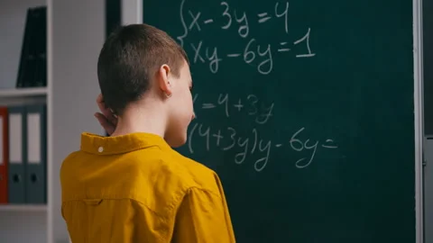 Teenage boy trying to solve math equation near chalkboard, scratching his head Stock Footage 251805694