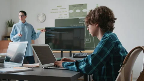 Teenage Boy Typing Code on his Laptop While Listening to IT Teacher in School Video stock 317641299