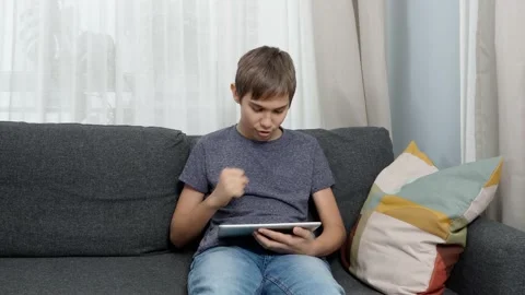 Teenage boy using digital tablet computer sitting on couch at home. Happy kid Stock Footage 166086638