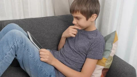 Teenage boy using digital tablet computer sitting on couch at home. Kid using Stock Footage 166163003
