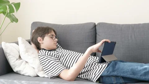 Teenage boy using digital tablet computer at home couch at home. Child looking Stock Footage 221258385