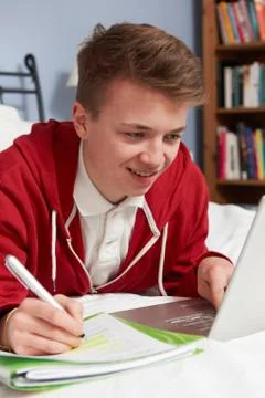 Teenage Boy Using Laptop For Homework In Bedroom Stock Photos