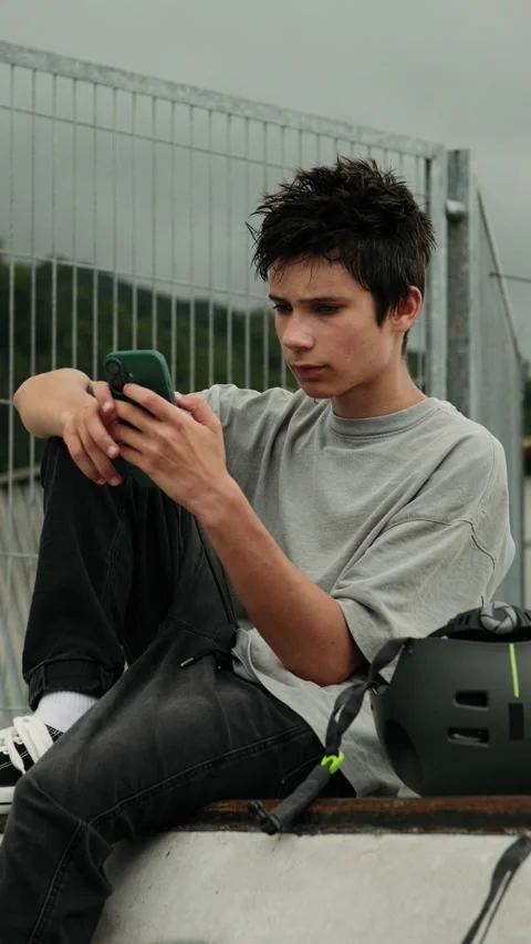 Teenage Boy Using a Smartphone While Sitting at a Skatepark Stock Footage 338074379