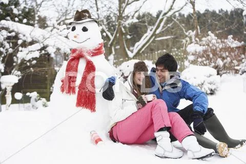 Teenage couple in winter landscape next to snowman with flask and hot drink Stock Photos