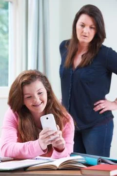 Teenage Daughter Using Mobile Phone Whilst Studying Stock Photos