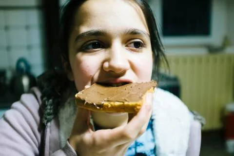 Teenage girl eats slice of bread with chocolate cream and hazelnuts for snack Stock Photos