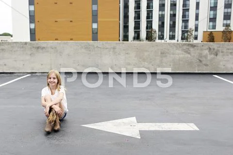 Teenage girl sitting on urban rooftop parking lot Stock Photos