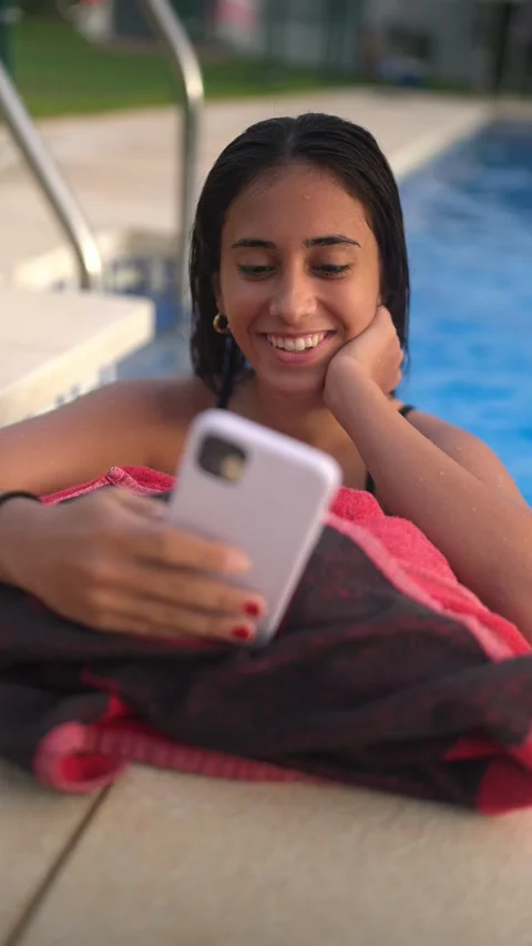 Teenage girl smiling while using her smartphone by the swimming pool Video stock 343736133