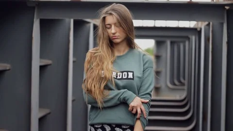 A teenage girl standing in a metal room with her eyes closed, pulling up her Stock Footage