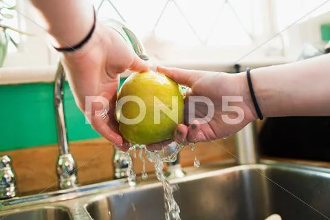 Teenage Girl Washing Apple In Kitchen Sink