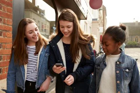 Teenage Girls Walking Along Street Looking At Social Media Stock Photos