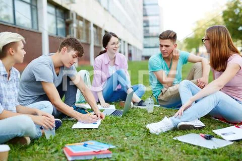 Teenage groupmats sitting on lawn of campus and carrying out homework Stock Photos