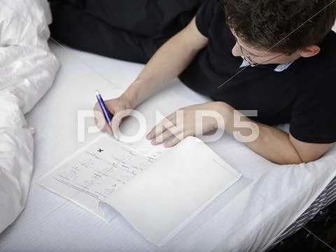 Teenage high school student studying, solving math problems in bed Stock Photos