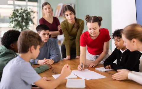 Teenage students solving problem on paper while teacher watches behind Stock Photos