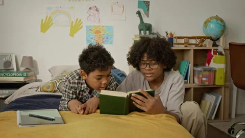 Teenager and Younger Brother Reading Book Together on Bed Stock Footage 342503553