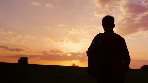 A teenager with a backpack over his shoulder goes towards the sunset in the Stock Footage